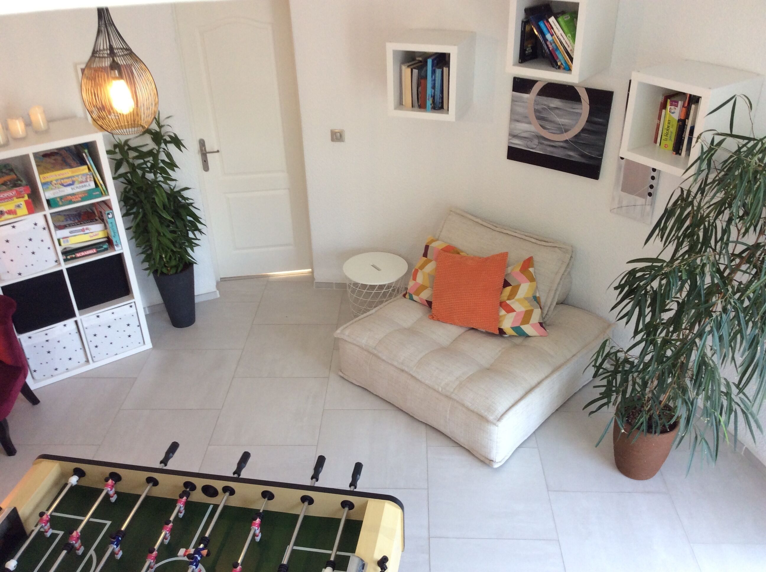 Una sala de estar acogedora con un sofá, una mesa de fútbol y una estantería.
