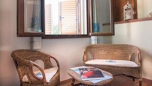 Una habitación con dos sillones de mimbre, una mesita con revistas y una ventana con persianas.
