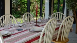 Une table à manger agrémentée de chaises blanches, de verres transparents et d’assiettes, avec une bougie rouge comme élément décoratif central.