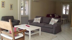 Un salon avec un canapé gris, une chaise en bois, une table basse blanche et une petite table sur laquelle se trouve un objet rouge.