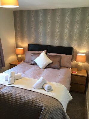 A neatly made bed with a brown quilt, two white pillows, and a headboard. There are two bedside lamps on wooden nightstands. - River View - Cosy country cottage. Ideal for a family and pets welcome. (Frosterley, County Durham)