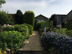 A garden pathway leading to a wooden house with a sloped roof. - River View - Cosy country cottage. Ideal for a family and pets welcome. (Frosterley, County Durham)