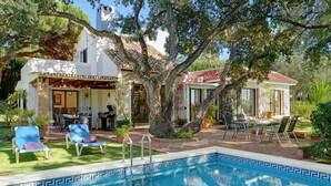Zona de piscina con un diseño geométrico de baldosas, mobiliario exterior y un gran árbol.
