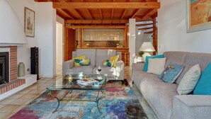 Una sala de estar con sofá, mesa de centro y chimenea. Se ve una cocina a través de un vano abierto.