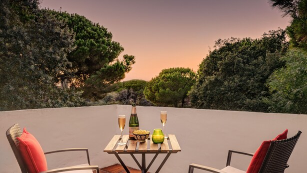 Una terraza con dos sillas, una mesa, una botella de champán y copas.