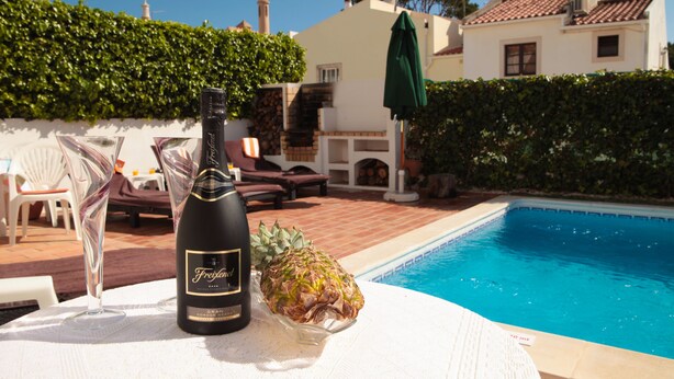 A bottle of Freixenet champagne, a pineapple, and a poolside setting with lounge chairs and a white wall. - Fantastic Villa With Private Pool In Vilamoura  (Vilamoura)