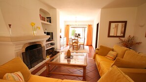 A living room with a fireplace, yellow sofas, a coffee table, and a dining area in the background. - Fantastic Villa With Private Pool In Vilamoura  (Vilamoura)