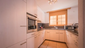 A compact kitchen with white cabinets, a built-in oven, a microwave, and a window with blinds.