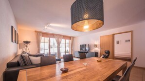 A modern living room with a wooden dining table, leather sofa, and a TV.