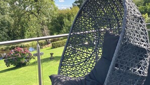A hanging chair with a woven seat and backrest, attached to a metal frame, on a deck with a metal railing. - Caithness Holiday Home (Pontypool)