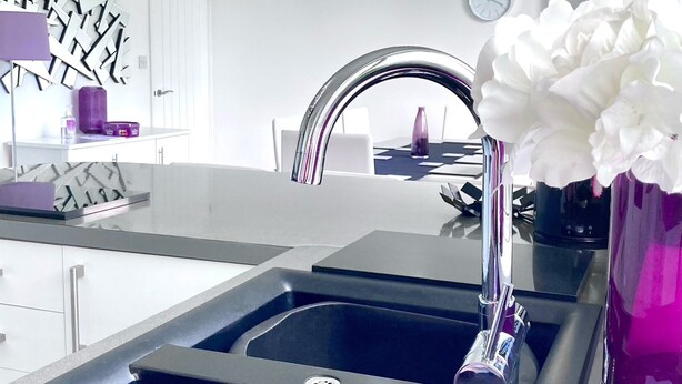 A modern kitchen with a double sink, a stainless steel faucet, and a vase with white flowers on the counter. - Caithness Holiday Home (Pontypool)