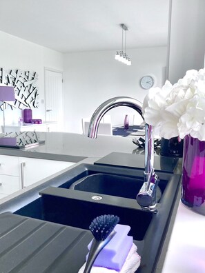 A modern kitchen with a double sink, a stainless steel faucet, and a vase with white flowers on the counter. - Caithness Holiday Home (Pontypool)