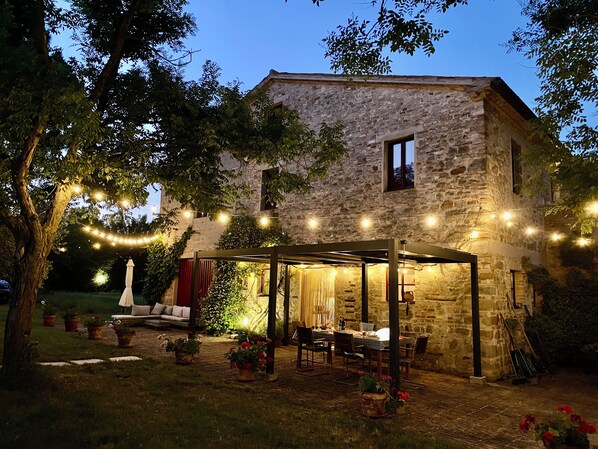 A stone building with a covered patio area, potted plants, and string lights. - Spacious ground floor apartment & Private Pool & large garden. wifi. Sleeps 8. (Cingoli)