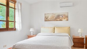 Een slaapkamer met een bed, twee nachtkastjes met lampen, een wandairconditioner, een spiegel en een raam met gordijnen.