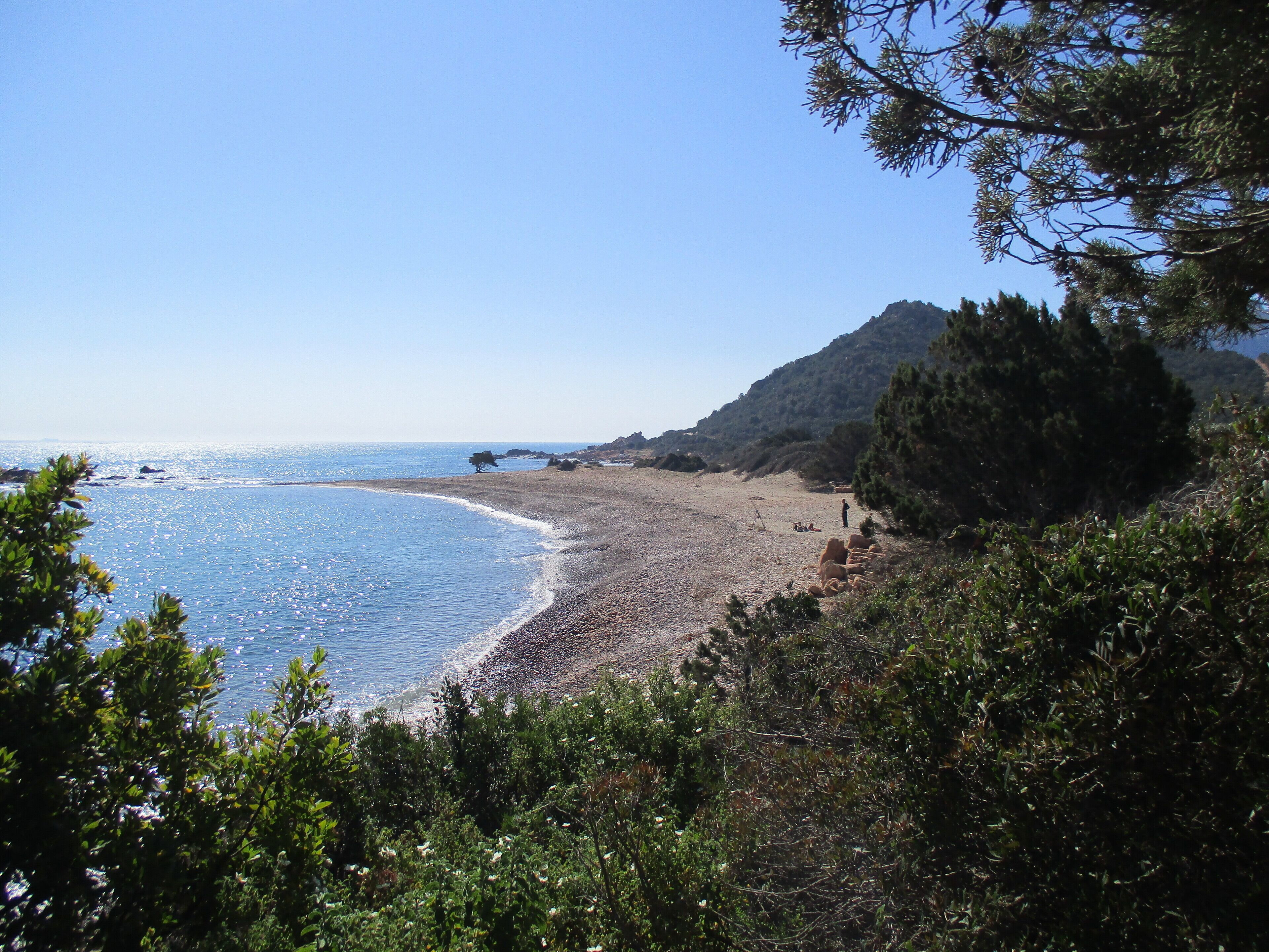 A beach with a rocky shoreline, a clear sky, and a mountain in the background.