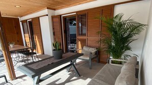 An outdoor patio area with a wooden ceiling, a table with chairs, a sofa, and a potted plant.