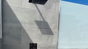 A wall-mounted showerhead with water spray, a window with a view of palm trees, and a tiled floor.