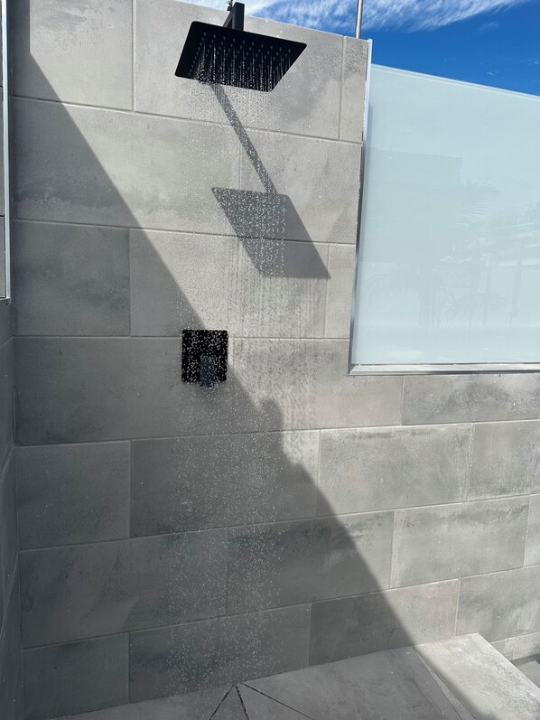 Un cabezal de ducha instalado en la pared, una ventana con vista a palmeras y un piso de baldosas.