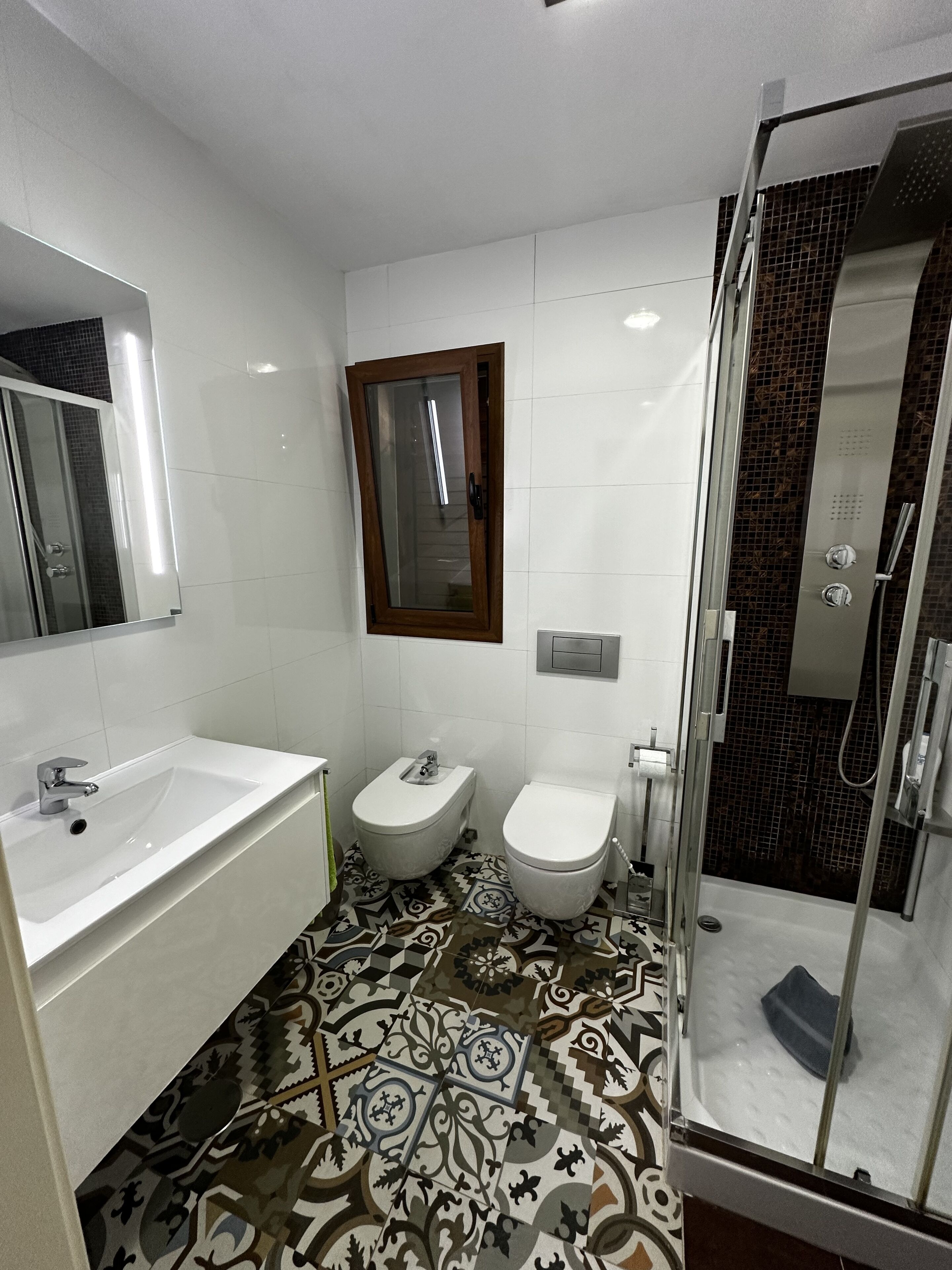 Un baño moderno con un espejo grande, un lavabo, un bidé y una zona de ducha.