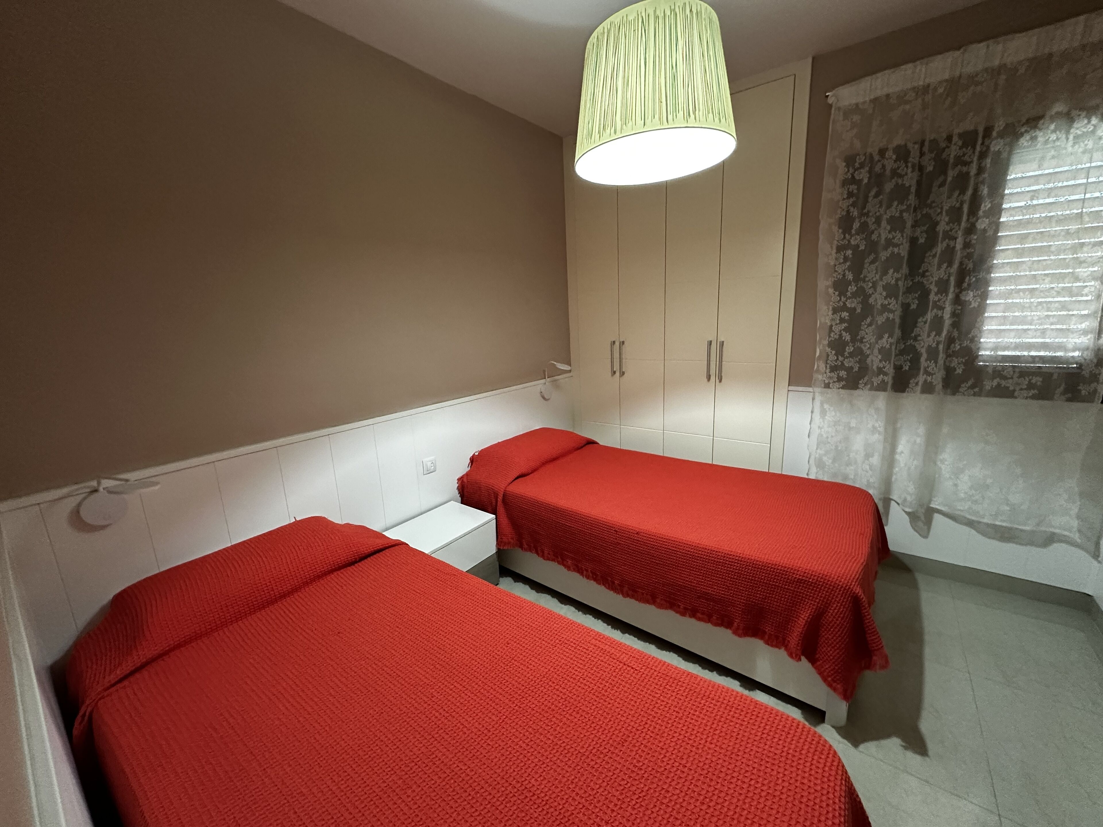A room with two beds, a wardrobe, and a window with curtains.