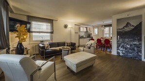 A modern living room with a sofa, ottoman, and red chairs. A dining area with a table and chairs is visible in the background. - High Standard Renovated Apartment for up to 8 persons, in the Centre (Zermatt)