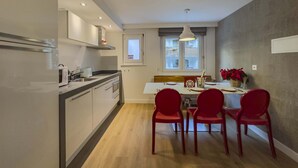 A modern kitchen with white cabinets, a microwave, and a dining area with red chairs and a table set for four. - High Standard Renovated Apartment for up to 8 persons, in the Centre (Zermatt)