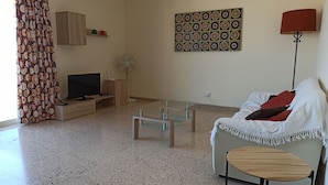 A living room with a TV, wooden cabinet, glass coffee table, and a couch with a white blanket. - Apartment with Sea View (Flat 5) (Triq L-Gherien, Mellieha)