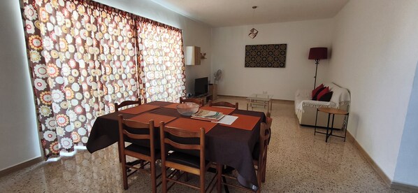 A dining area with a table set for four, chairs, a sofa, a TV, and a wall-mounted decorative item.