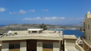 A building with a flat roof, a small tower-like structure, and a view of the sea and distant hills. - Apartment with Sea View (Flat 5) (Triq L-Gherien, Mellieha)
