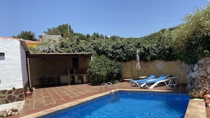 A swimming pool with two sun loungers, a stone wall, and a small covered seating area. - House in a very quiet rural area with easy accessibility. 3.5 km from the beach (Cajiz)