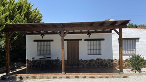 A covered patio area with a table and chairs, a wooden pergola, and a white building with stone accents. - House in a very quiet rural area with easy accessibility. 3.5 km from the beach (Cajiz)