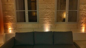 A dark-colored sofa with three cushions against a textured wall with three windows. - STANDING APARTMENT, from the 18th Century, in the pedestrianized historic center (Montpellier)