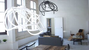 A spacious room with a high ceiling, a wooden dining table, a grey sofa, and a hanging light fixture. - STANDING APARTMENT, from the 18th Century, in the pedestrianized historic center (Montpellier)