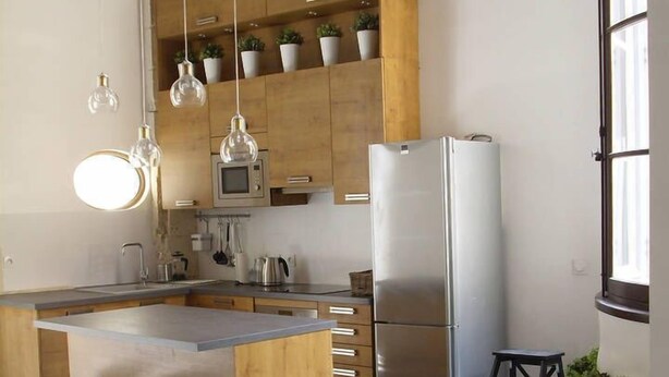 A modern kitchen with wooden cabinets, a stainless steel refrigerator, and hanging pendant lights. - STANDING APARTMENT, from the 18th Century, in the pedestrianized historic center (Montpellier)