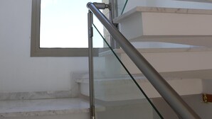 A modern staircase with glass railings and a view of the sky through a large window.