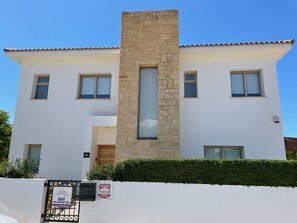 A two-story villa with a stone facade, multiple windows, and a well-maintained hedge.