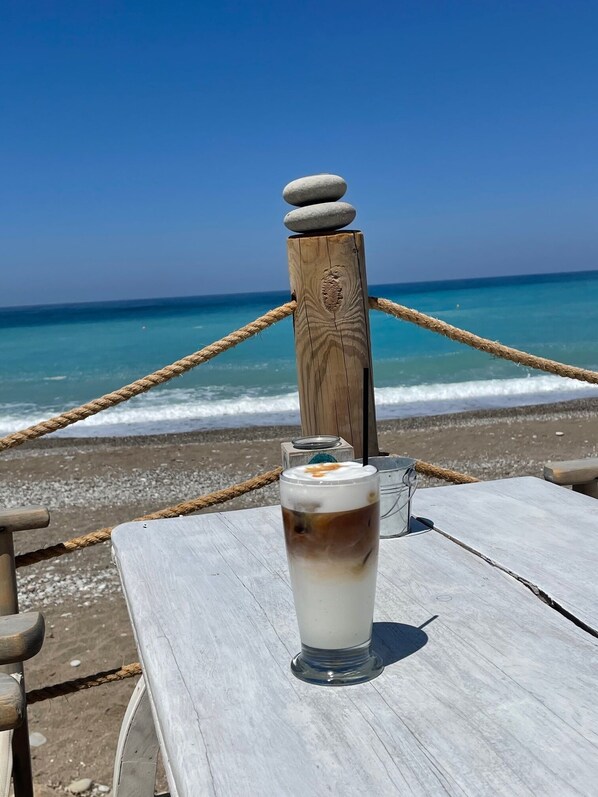 A glass of iced coffee on a wooden table by the beach with a rope barrier and a wooden post in the background. - Fab 3 Bed 3 Bath Villa, Large heated 10M Pool .Pool Heating  40 euros per day (Coral Bay)