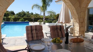 An outdoor dining area with a pool view, stone arches, and striped chairs.