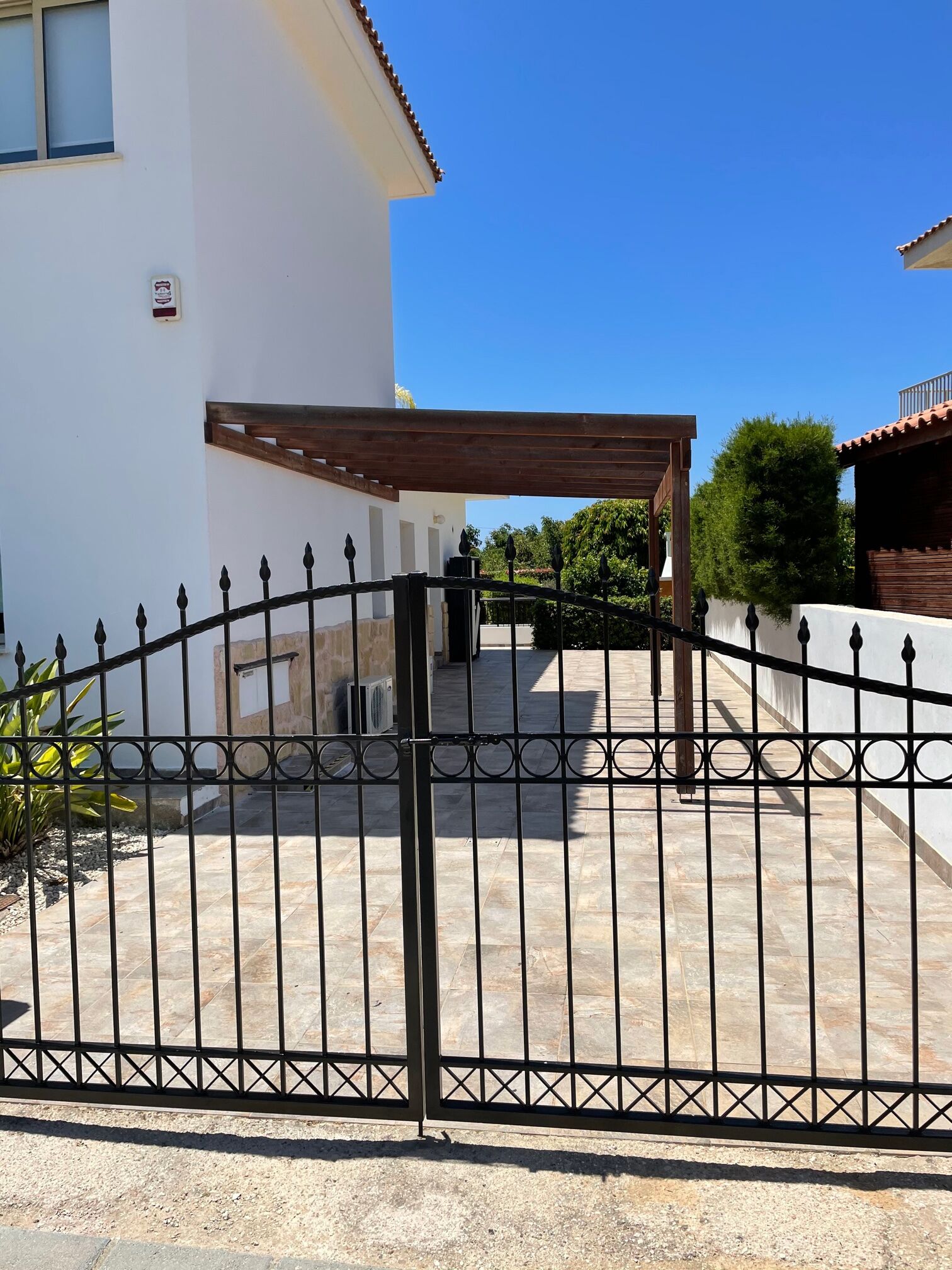 A gated entrance to a property with a pergola, a white building, and a clear blue sky.