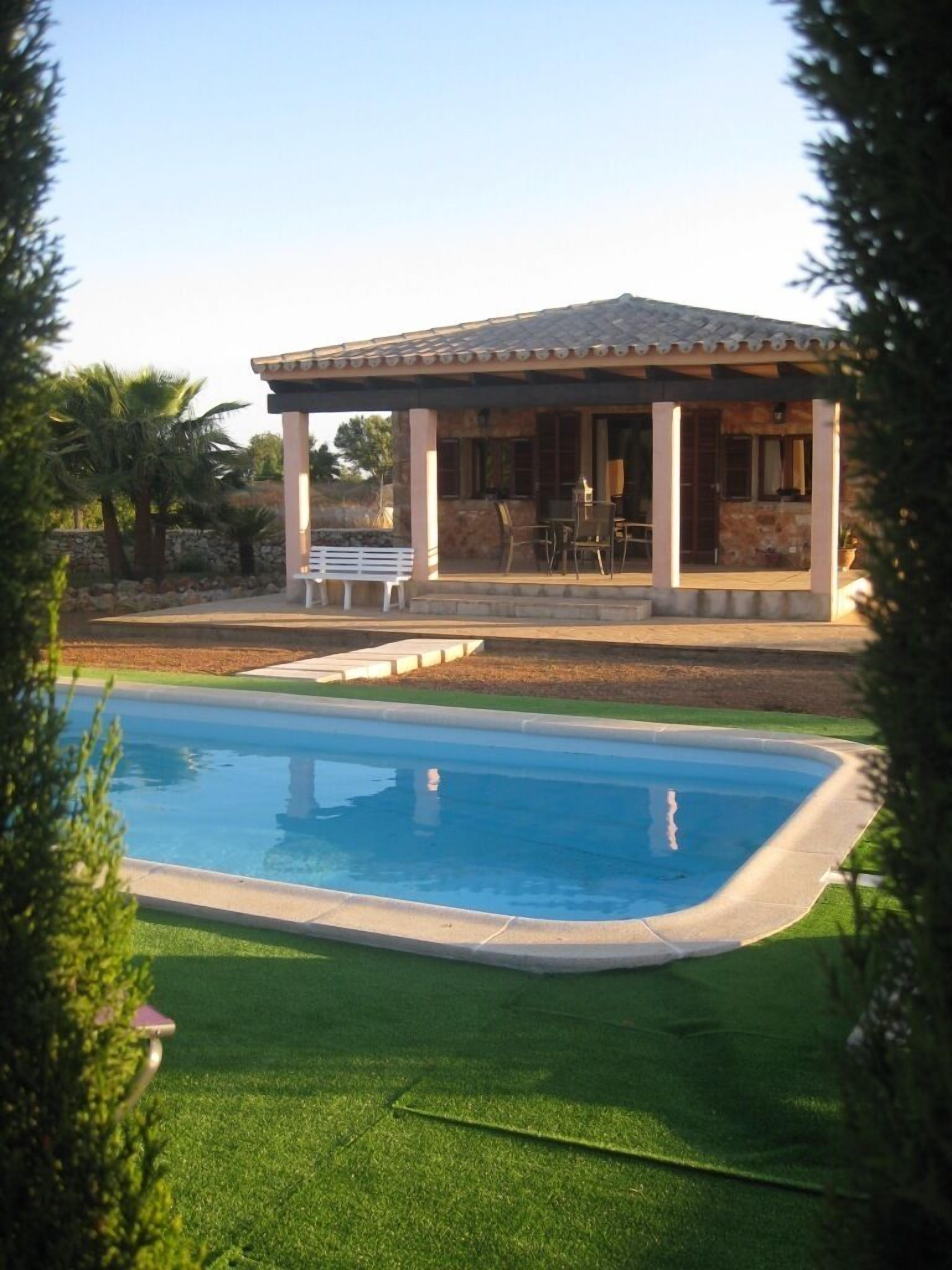 A poolside area with a covered patio, a stone building, and a lawn.