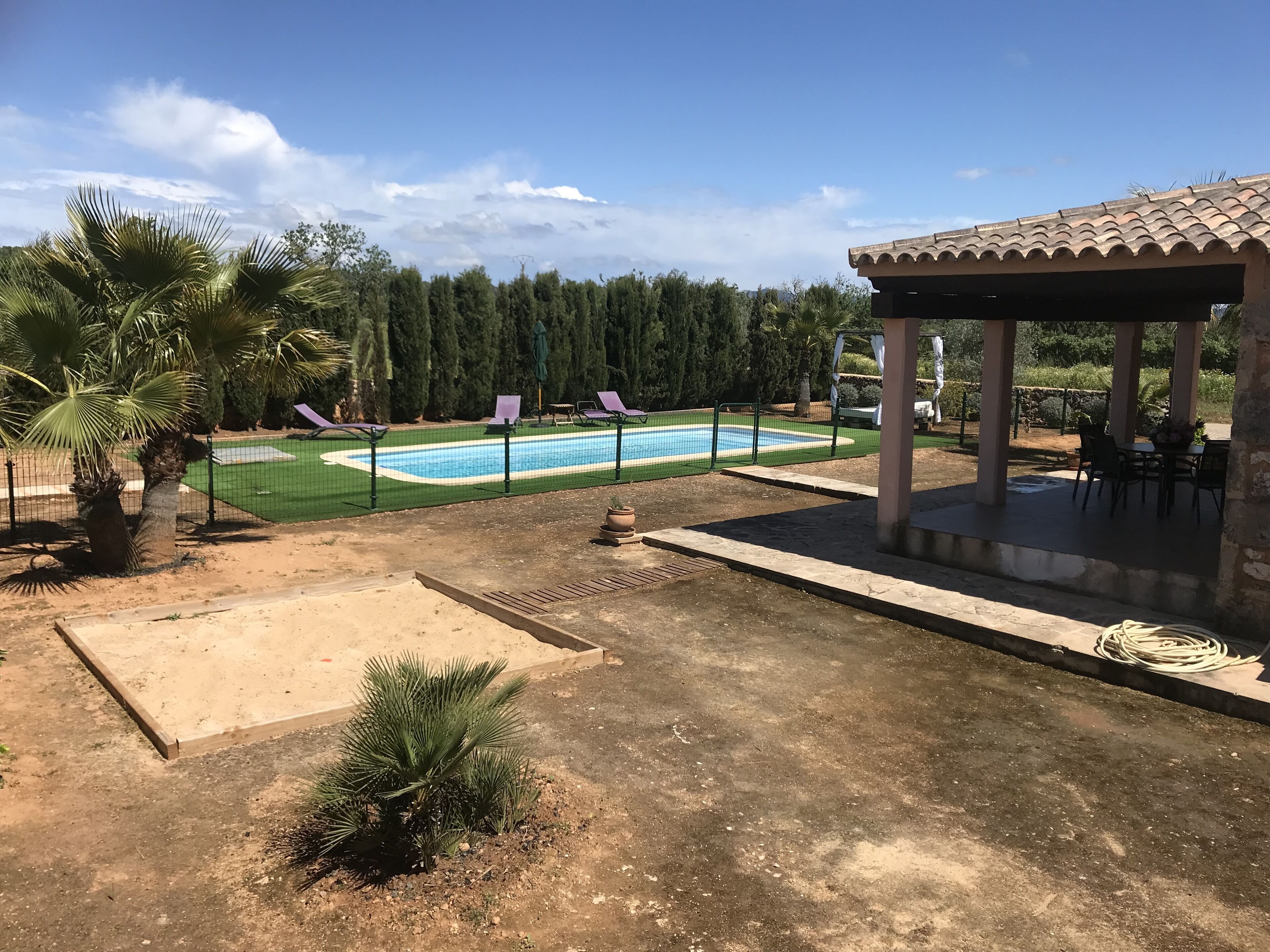 A pool area with a fenced swimming pool, lounge chairs, and a covered seating area.