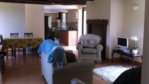 A living room with a sofa, armchair, and a television on a stand. There is a dining table with chairs and a kitchen area in the background. - Renovated Traditional Stone House With Private Salt Water Pool  (Gourdon)