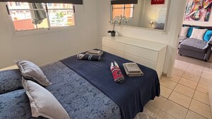 Un dormitorio con cama, cómoda, espejo, ventilador de techo y ventana.
