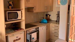 Una cocina compacta con armarios de madera, un microondas, un lavavajillas y un horno pequeño.