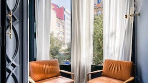 A room with two leather chairs and a round table, a window with white curtains, and a view of buildings outside. - Luxury Apartment on Valencia Street (Barcelona)
