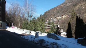 Eine verschneite Straße mit einem Gebäude links und einem Berg mit Häusern im Hintergrund.