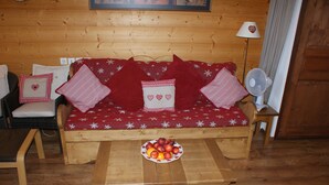 Ein gemütliches Zimmer mit einer Holzdavaya, einem Holztisch mit Obst und einem Ventilator.