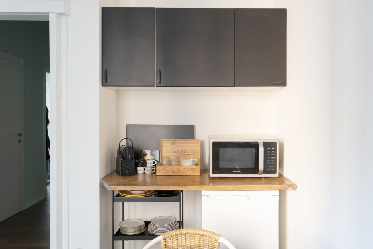 A compact kitchen with a microwave, a wooden box, and a basket on a shelf.