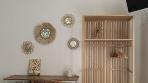 A room with a wooden desk, wicker chair, and a wooden shelving unit with a hanging garment. - Happy Travelers Apartment (Como)