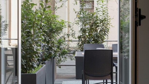 A balcony with a table and chairs, surrounded by potted plants. - Happy Travelers Apartment (Como)